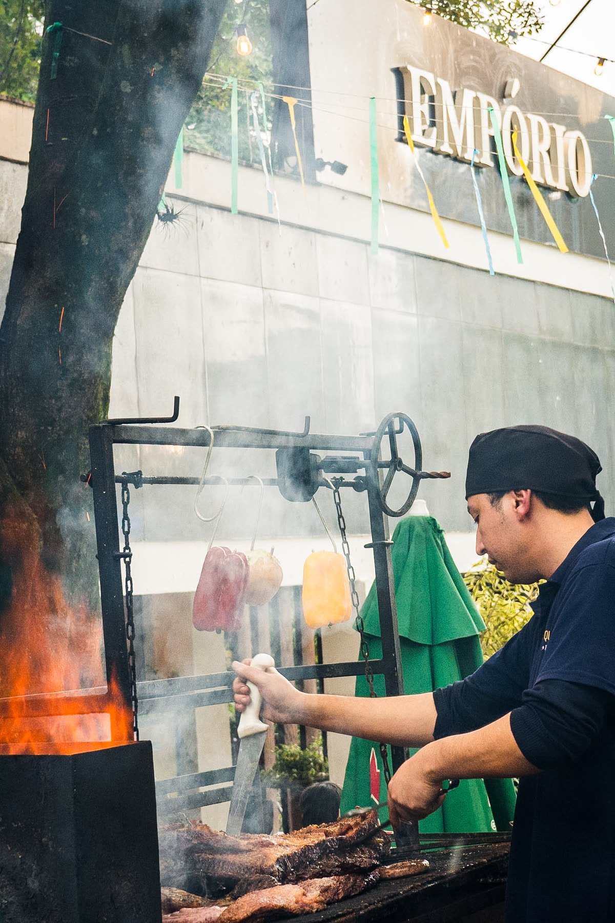 Cozinheiro cuidando da brasa em frente ao letreiro Empório