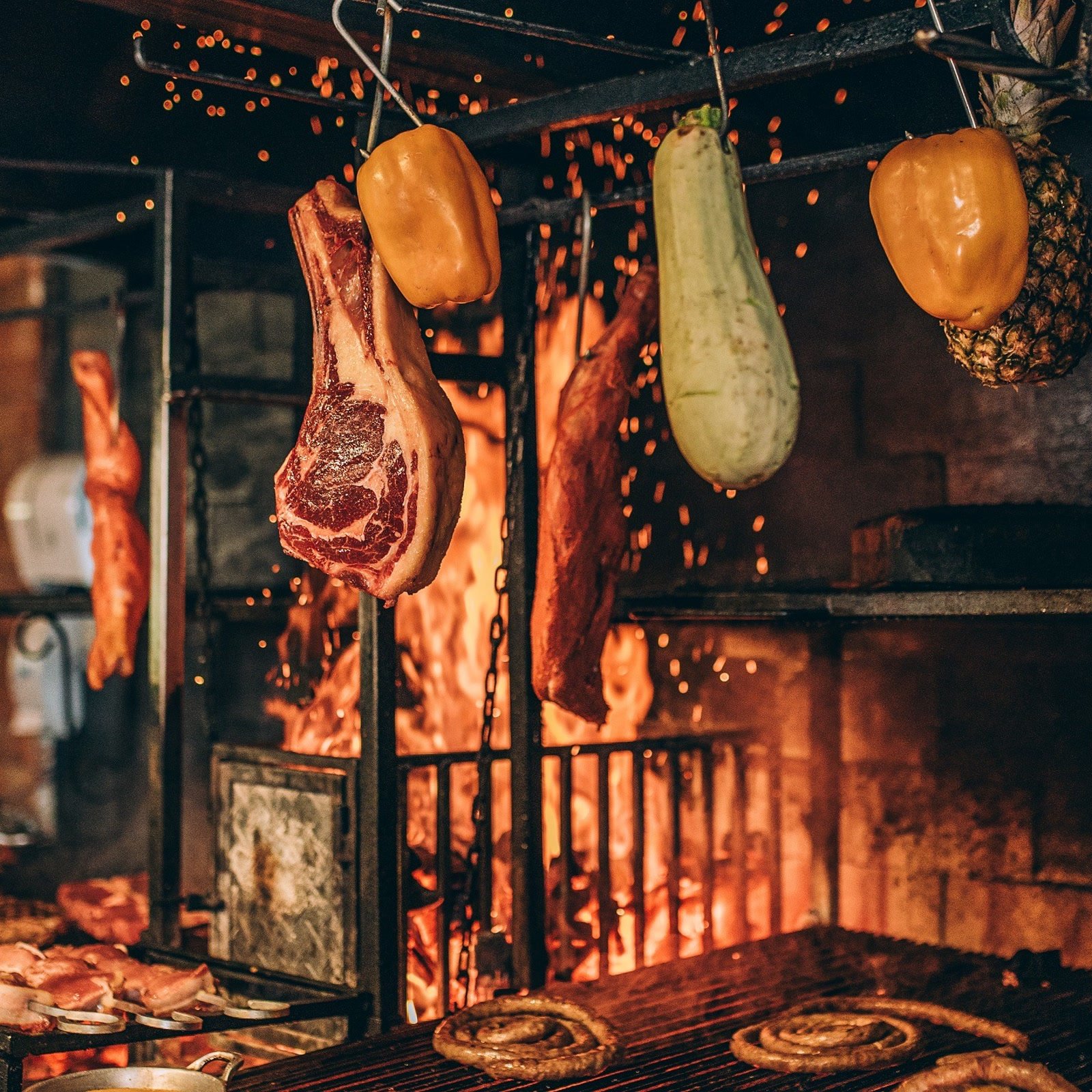 Cortes e legumes na brasa da parrilla, com fogo intenso e brasas ao fundo
