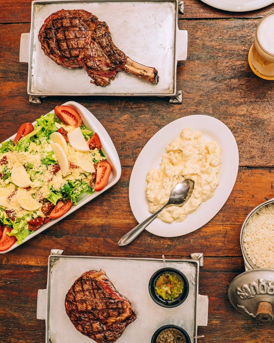 Mesa com assado de tira, salada e acompanhamentos da parrilla